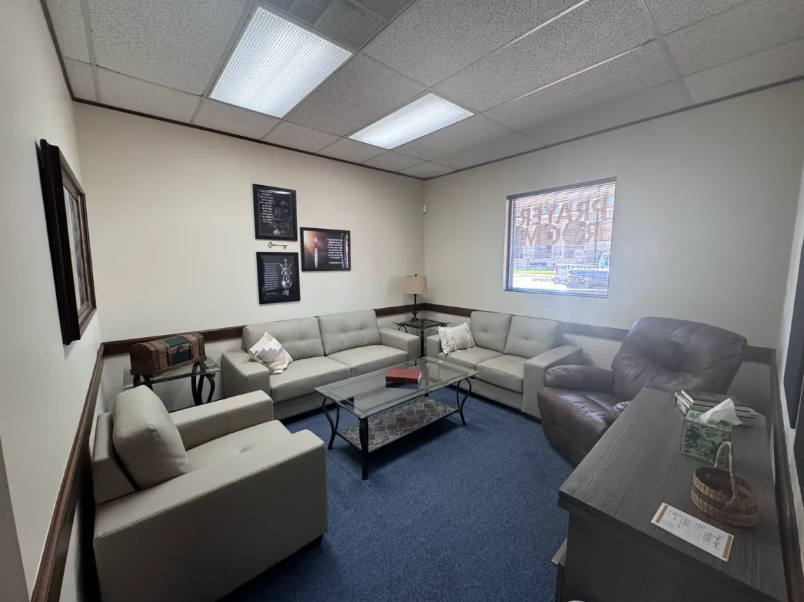 The Intercessor Room at the Seek the City prayer room — sofas and armchairs around a low table, framed prints on the walls, and the prayer room’s window lettering behind.