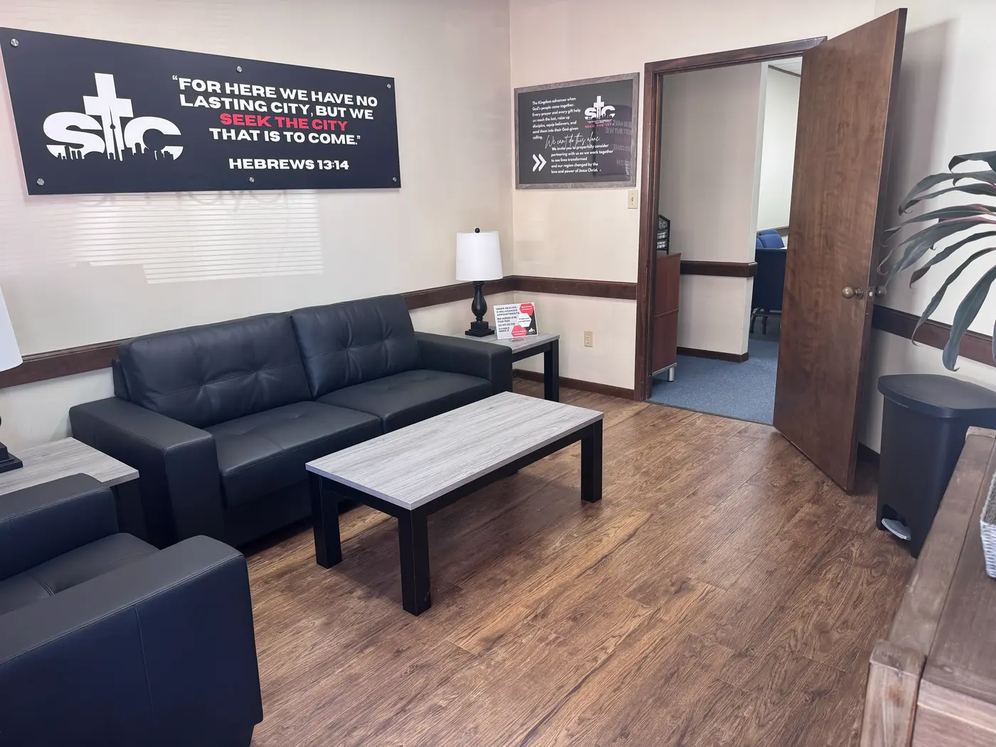The entry lounge at the Seek the City prayer room — leather seating and a coffee table beneath a banner reading “For here we have no lasting city, but we seek the city that is to come. Hebrews 13:14”.