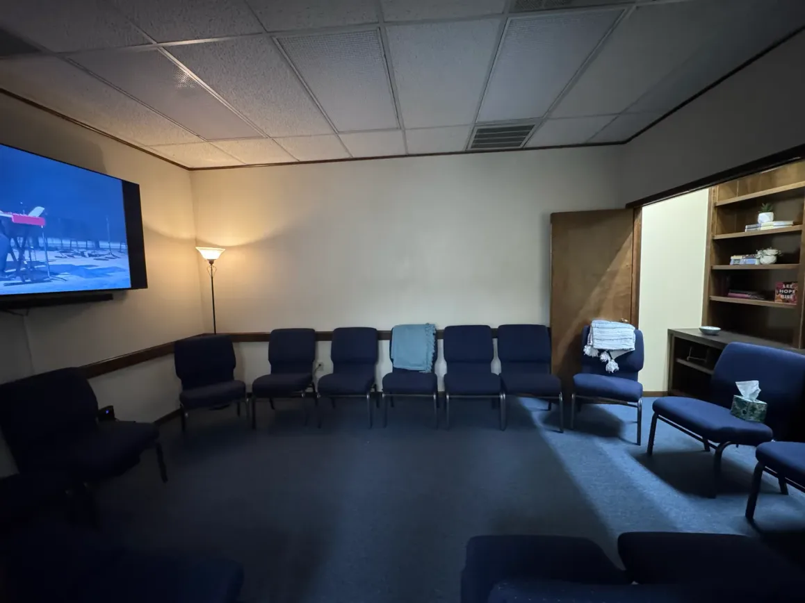 The Soaking Room at the Seek the City prayer room — dimly lit with a floor lamp, a ring of chairs, worship playing on a wall screen, and a small bookshelf.