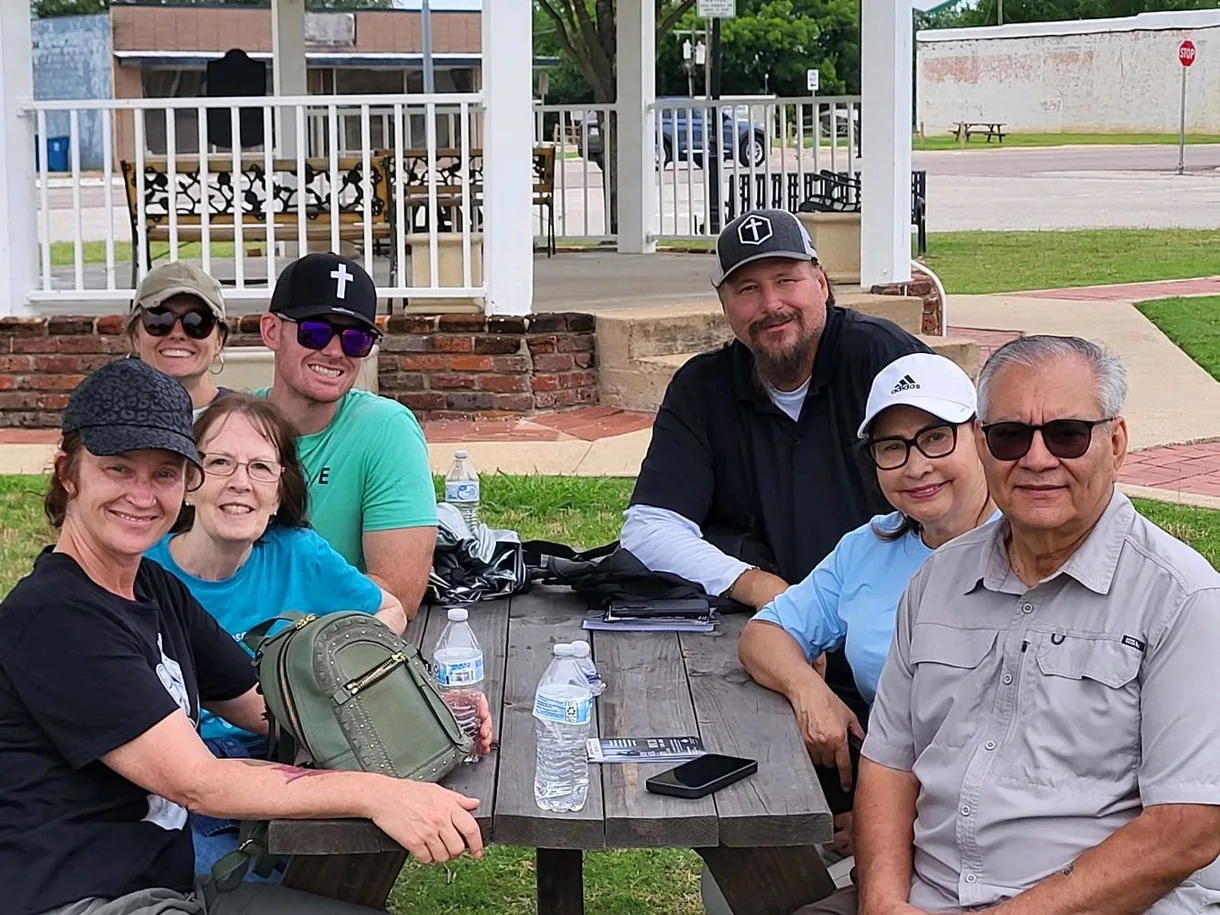 Wayne and a group from Seek the City gathered around a picnic table in a Cleburne park, smiling together after an outreach.